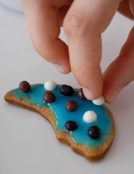 main d'enfant posant une petiet décoration en sucre sur un petit sablé coloré avec du sucre alimentaire coloré
